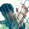 Young man holding onto chain link fence