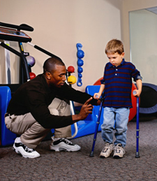 health care provider helping child walk with crutches through physical therapy
