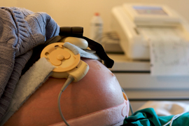 A close-up of a pregnant belly with a fetal monitor attached.