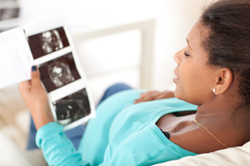 Pregnant woman sitting on the couch in the living room and looking at her ultrasound scan of the fetus.